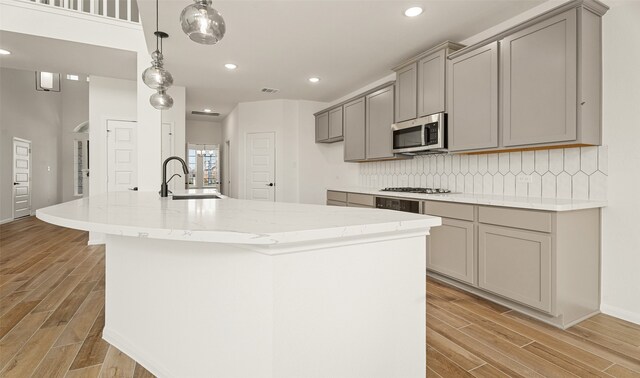 kitchen with gray cabinetry, pendant lighting, a kitchen island with sink, and light hardwood / wood-style flooring