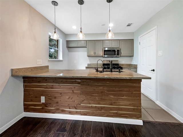 kitchen with stainless steel appliances, hanging light fixtures, kitchen peninsula, and dark hardwood / wood-style flooring