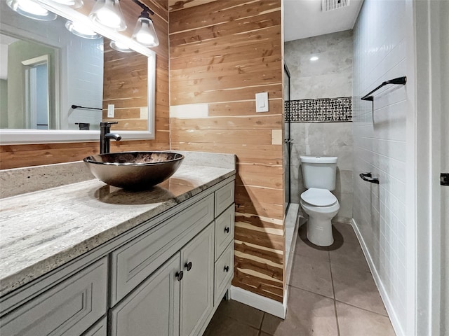 bathroom featuring toilet, tile patterned flooring, wooden walls, vanity, and a shower