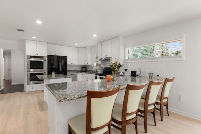 kitchen featuring white cabinets, kitchen peninsula, light hardwood / wood-style flooring, a breakfast bar area, and appliances with stainless steel finishes