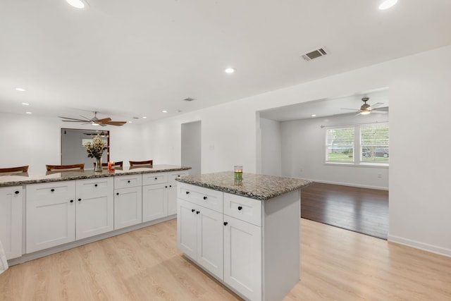 kitchen featuring dark stone countertops, a kitchen island, white cabinetry, and light wood-type flooring