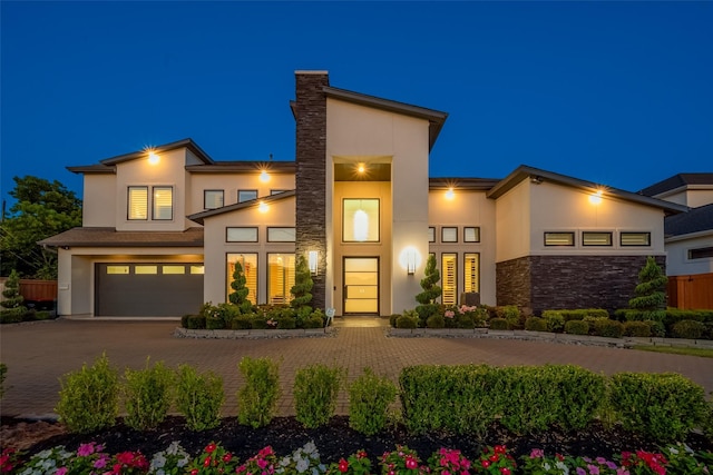 contemporary house with an attached garage, stone siding, decorative driveway, and stucco siding