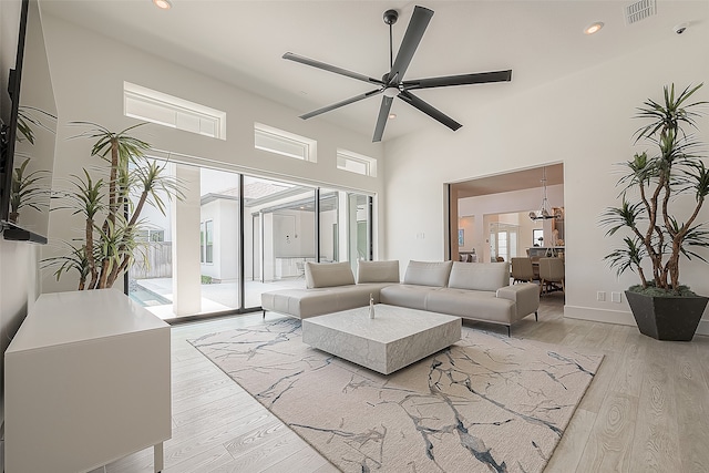 living room with light wood-type flooring, ceiling fan, and a towering ceiling