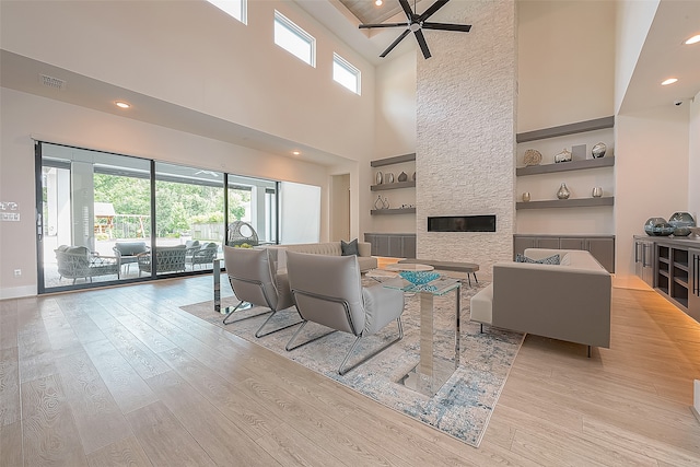 living room featuring ceiling fan, light wood-type flooring, a towering ceiling, and a fireplace