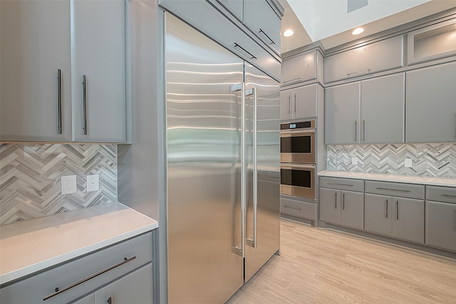 kitchen with gray cabinets, light countertops, light wood-style flooring, decorative backsplash, and appliances with stainless steel finishes