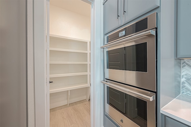 kitchen with gray cabinets, light wood-type flooring, double oven, and tasteful backsplash