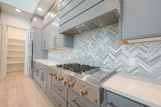 kitchen with premium range hood, backsplash, light hardwood / wood-style flooring, and gray cabinetry