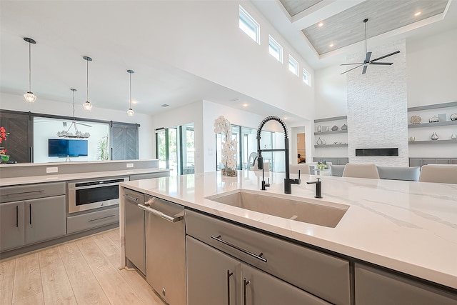 kitchen with light stone countertops, hanging light fixtures, sink, light wood-type flooring, and gray cabinets