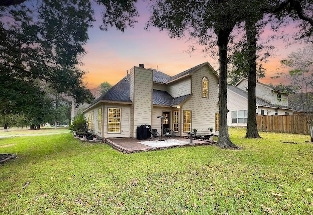 back house at dusk featuring a lawn and a patio area