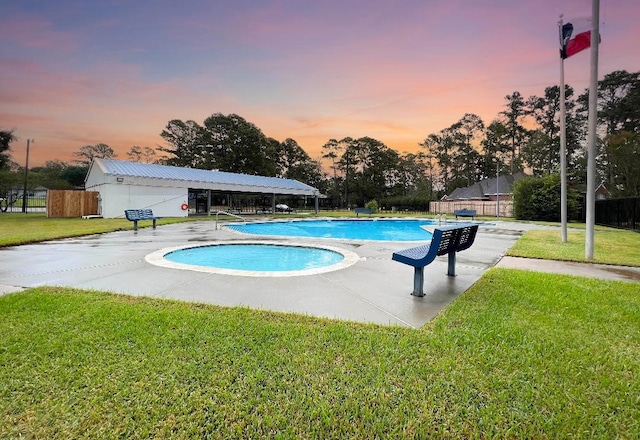 pool at dusk featuring a patio and a lawn