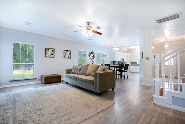 living room with hardwood / wood-style floors, ceiling fan with notable chandelier, crown molding, and decorative columns