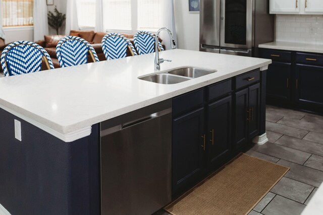 kitchen with sink, stainless steel appliances, backsplash, an island with sink, and light tile patterned flooring