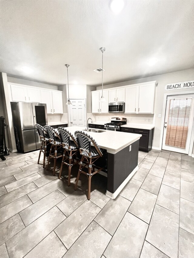 kitchen with stainless steel appliances, a kitchen island with sink, white cabinetry, hanging light fixtures, and a breakfast bar area