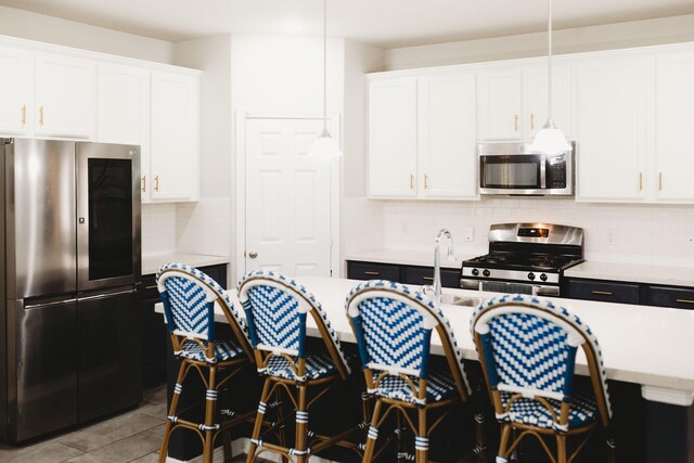 kitchen featuring a kitchen island with sink, hanging light fixtures, decorative backsplash, white cabinetry, and stainless steel appliances