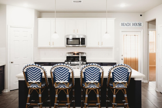 kitchen with white cabinetry, an island with sink, stainless steel appliances, and decorative light fixtures