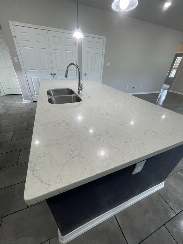 kitchen with light stone countertops, an island with sink, hanging light fixtures, and sink