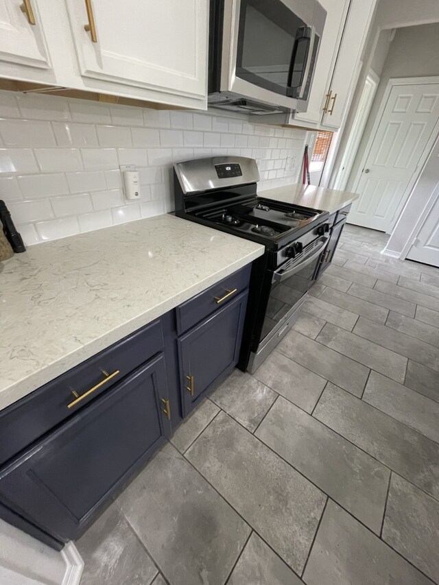 kitchen featuring light stone countertops, tasteful backsplash, stainless steel appliances, blue cabinets, and white cabinets