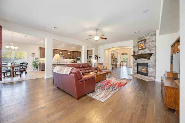 living room featuring a stone fireplace, dark hardwood / wood-style floors, and ceiling fan with notable chandelier