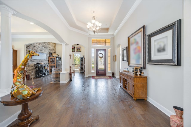 foyer entrance featuring ornamental molding, dark hardwood / wood-style floors, an inviting chandelier, a raised ceiling, and decorative columns