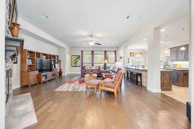 living room featuring light wood-type flooring, a fireplace, and ceiling fan