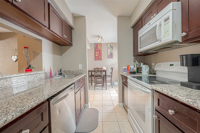 kitchen with light tile patterned floors, white appliances, sink, and light stone counters