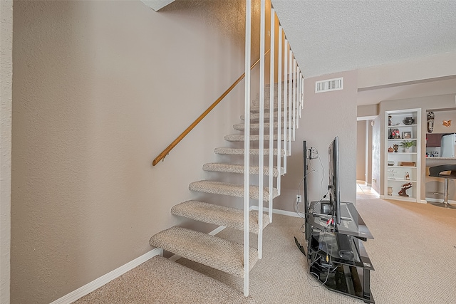 staircase with a textured ceiling and carpet flooring