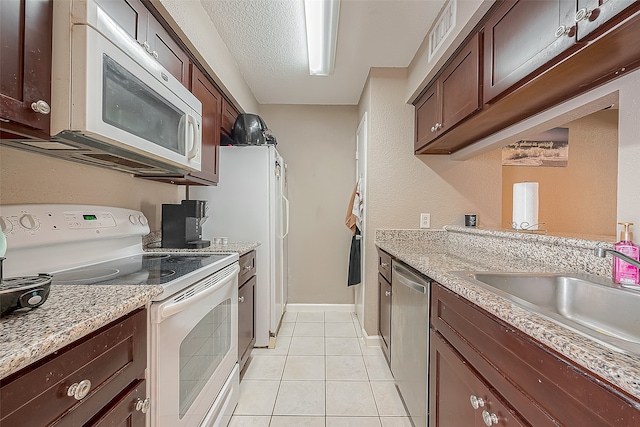 kitchen featuring light tile patterned flooring, a textured ceiling, light stone countertops, sink, and white appliances