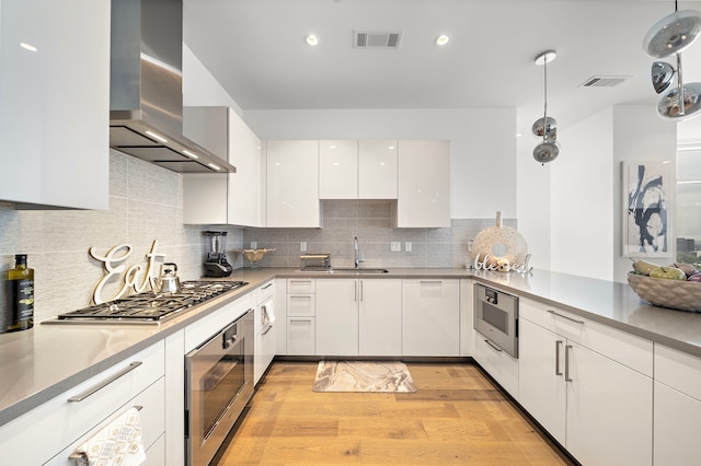 kitchen featuring white cabinetry, appliances with stainless steel finishes, sink, light hardwood / wood-style floors, and wall chimney exhaust hood