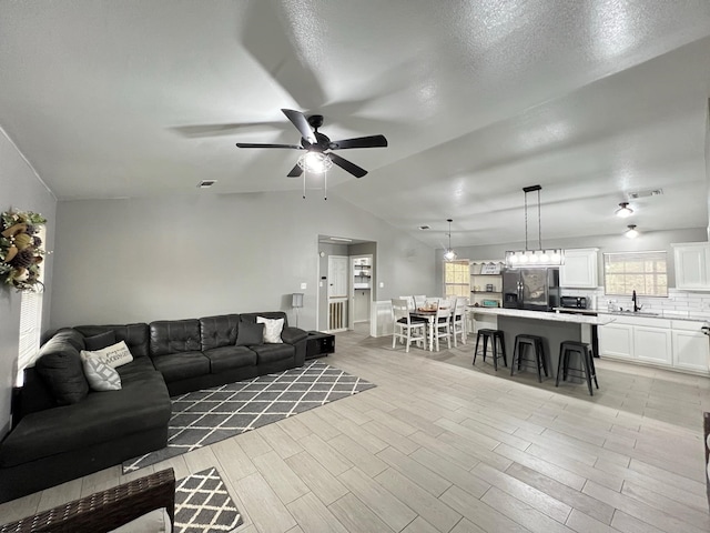 living room featuring sink, vaulted ceiling, ceiling fan, a textured ceiling, and light hardwood / wood-style floors