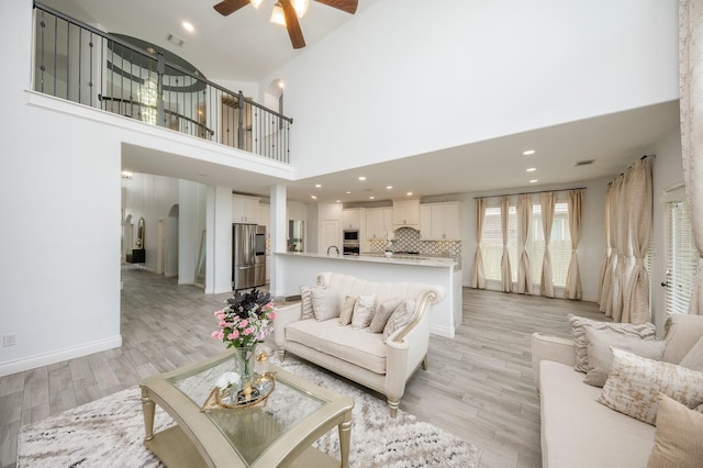 living room with a high ceiling, ceiling fan, and light hardwood / wood-style flooring