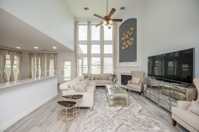 living room featuring light hardwood / wood-style floors, a healthy amount of sunlight, a high ceiling, and ceiling fan