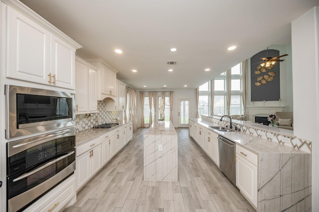 kitchen featuring light stone counters, white cabinetry, appliances with stainless steel finishes, light hardwood / wood-style floors, and ceiling fan