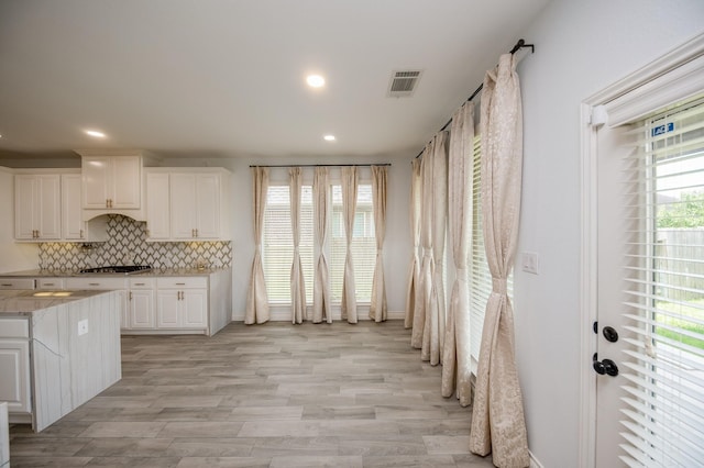 kitchen featuring light stone countertops, white cabinetry, decorative backsplash, and light hardwood / wood-style floors