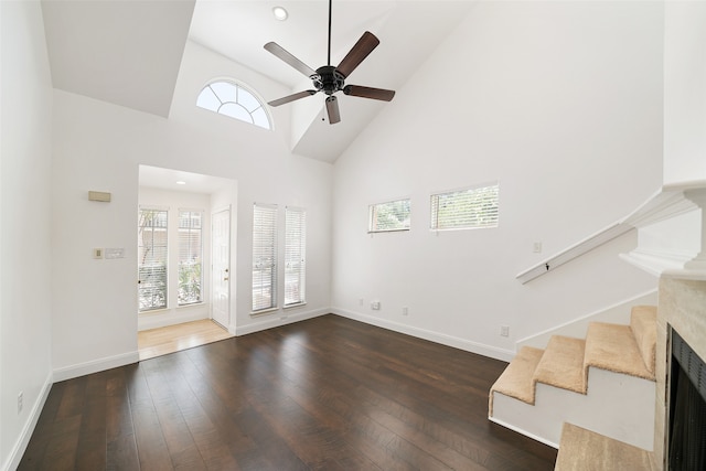 unfurnished living room featuring dark wood-type flooring, ceiling fan, high vaulted ceiling, and a high end fireplace