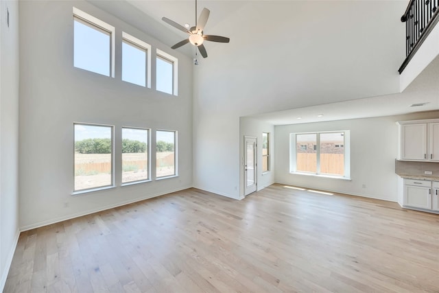 unfurnished living room with plenty of natural light, light wood-type flooring, and a towering ceiling