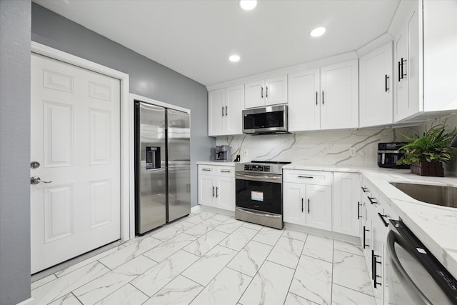 kitchen with tasteful backsplash, light stone countertops, appliances with stainless steel finishes, and white cabinets