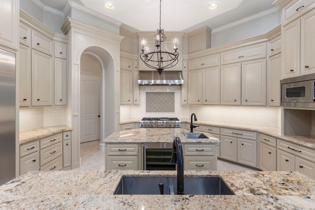 kitchen with pendant lighting, sink, built in appliances, light stone countertops, and cream cabinetry