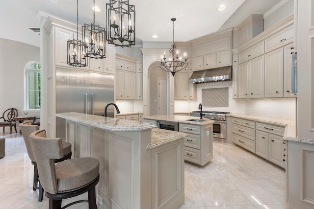 kitchen with hanging light fixtures, premium appliances, tasteful backsplash, a breakfast bar, and a center island with sink