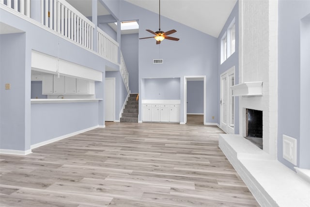 unfurnished living room with high vaulted ceiling, light wood-type flooring, ceiling fan, and a brick fireplace