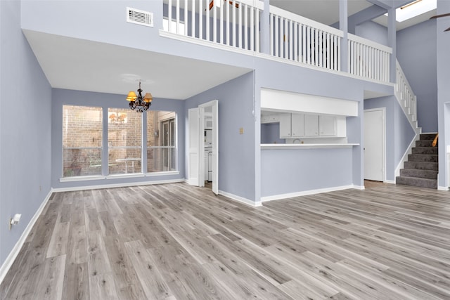 unfurnished living room featuring light wood-type flooring, a high ceiling, and an inviting chandelier