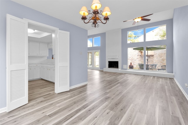 unfurnished living room with a towering ceiling, light wood-type flooring, a large fireplace, and ceiling fan with notable chandelier