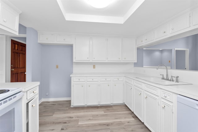 kitchen with sink, a tray ceiling, white appliances, white cabinets, and light wood-type flooring