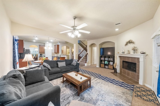 living room featuring ceiling fan with notable chandelier, a tile fireplace, and carpet flooring