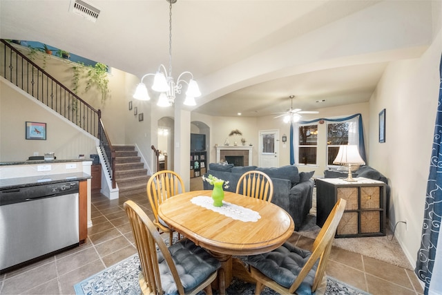 tiled dining area with a fireplace and ceiling fan with notable chandelier