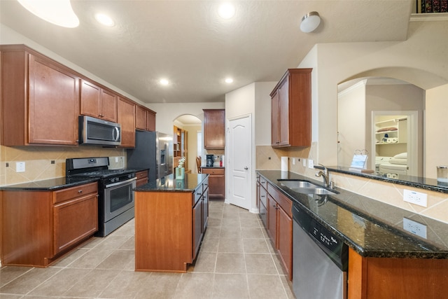 kitchen with sink, light tile patterned floors, a kitchen island, appliances with stainless steel finishes, and dark stone countertops