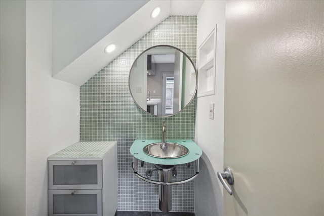 bathroom featuring tile walls, lofted ceiling, and sink