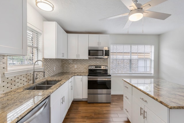 kitchen with light stone countertops, white cabinetry, sink, dark wood-type flooring, and appliances with stainless steel finishes