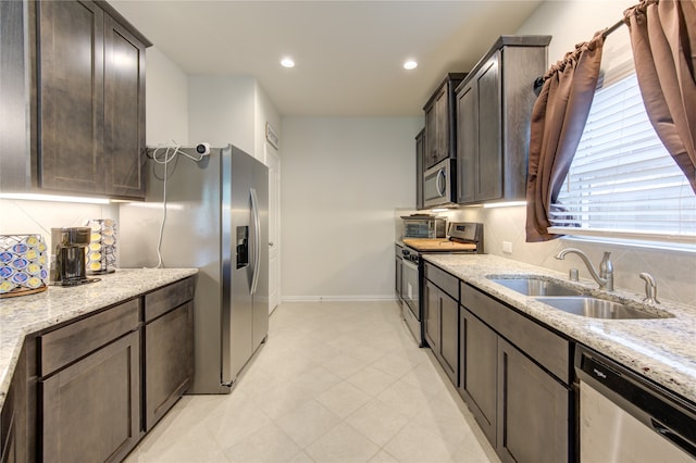 kitchen with sink, tasteful backsplash, light stone countertops, dark brown cabinets, and appliances with stainless steel finishes