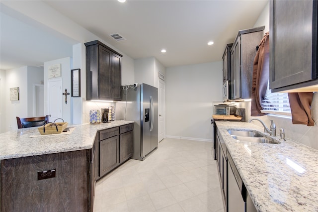 kitchen featuring light stone countertops, stainless steel refrigerator with ice dispenser, sink, and dark brown cabinetry