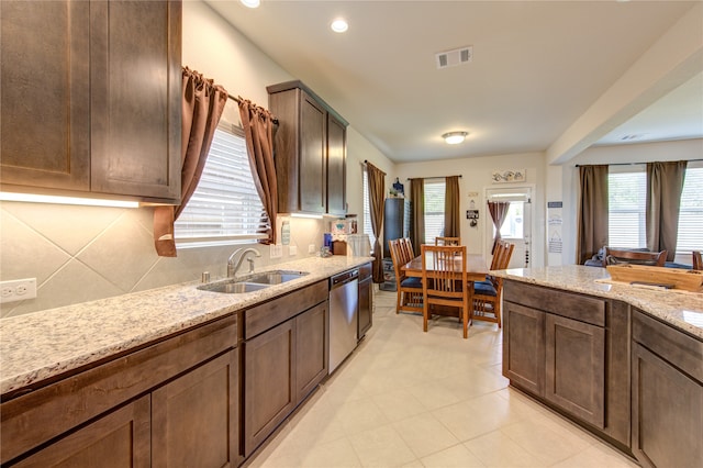 kitchen featuring tasteful backsplash, stainless steel dishwasher, sink, and light stone countertops